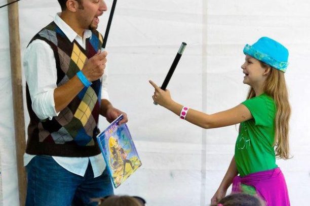 Man and girl performing a magic trick with wands in front of an audience.